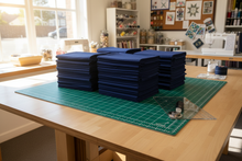 Load image into Gallery viewer, bundles of kona cotton navy colour on cutting,sewing table