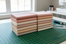 Load image into Gallery viewer, 12 piece kona cotton solids bundle called Blushing Bouquet layed on a cutting table
