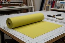Load image into Gallery viewer, Bolt of grellow kona cotton on a cutting table
